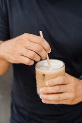manos removiendo un vaso de cristal con cafe con leche frio con hielo ice latte