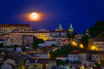 Fototapeta na wymiar Big full moon in clear night sky over old houses of Lisbon, Portugal