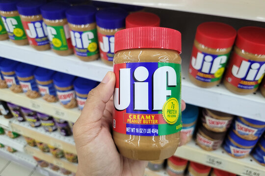 PENANG, MALAYSIA - 12 OCT 2023: An adult's hand holds a JIF brand peanut butter spread in a grocery store in Penang. Jif is an American brand of peanut butter made by The J.M. Smucker Company.