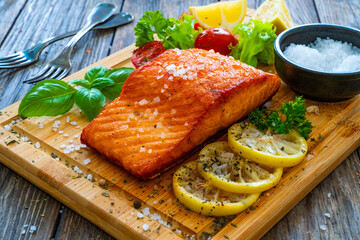 Seared salmon steak with lettuce, tomatoes and lemon on wooden table
