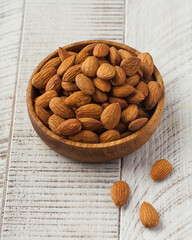 Dried peeled almonds on a wooden plate on a white wooden background. Nut 