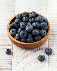 Juicy ripe blueberries in a wooden plate on a white wooden background. Berries.