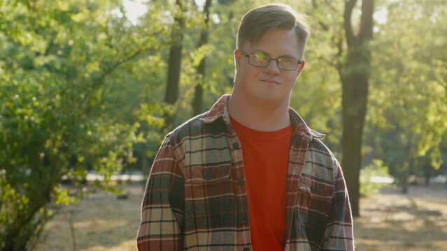 Portrait of young man with down syndrome in checkered shirt walking outdoors in the public park. Man with trisomy 21 illness. Disabled guy having a walk