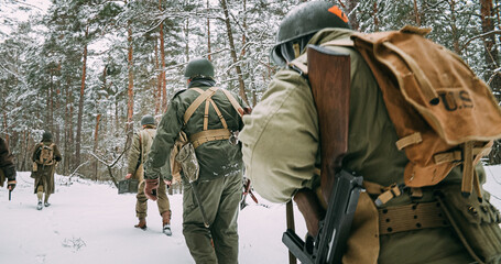 Heroes Of War. Re-enactors Dressed As American Infantry Soldier Marching Through Forest Road In Cold Winter Day. Group Of Usa Soldiers Marching Country Road. Usa Army Soldiers Of World War Ii.