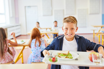 Happy schoolboy holding food tray in cafeteria