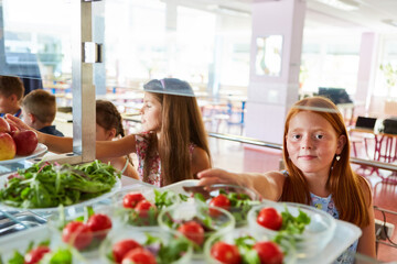 Girl taking vegetable salad from tray during lunch time