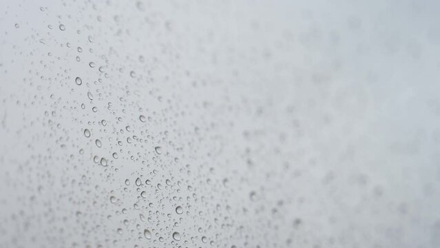 Close-up view of a rainy glass as rain drops hits a window during a gloomy and overcast weather.