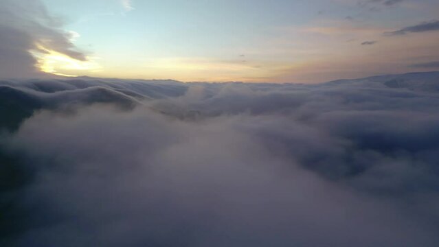 Drone video. The camera pans above the clouds, with a view of high snowy mountains covered in a dense haze encircling them. Against a blue sky with clouds at dawn. Armenia, Lori.