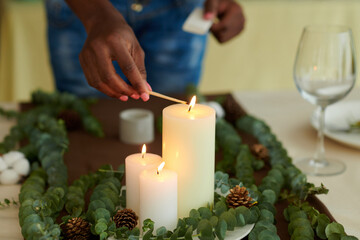 Closeup image of Black woman lightning thick candles on dinner table for Christmas celebration
