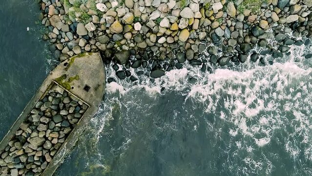 Top down drone view of waves hitting hte shore and some old barges