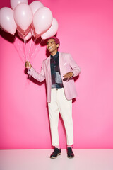 handsome young man with pink hair posing with pink balloons gesturing unnaturally, acting like doll
