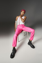 Fototapeta na wymiar african american male model in pink pants with suspenders posing on white chair, fashion concept