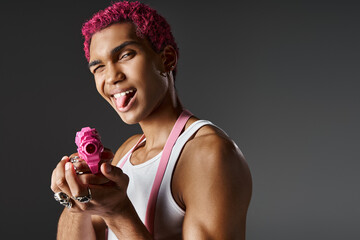 playful pink haired male model sticking out his tongue and leveling his pink toy gun at camera
