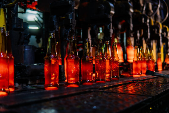 Production of glass bottles and glass containers. The heated glass bottles melted from quartz sand move along a conveyor line at a glass container plant. Working atmosphere with copy space.