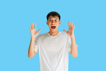 Young Asian man in white t-shirt having a big surprise, isolated on blue background. The concept of the arrival of big luck. Clipping Path