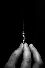 female hand elegantly holding an ink pen with a metal tip close-up on a black background. classic fountain pen isolated macro black and white. copy space. vertical - obrazy, fototapety, plakaty