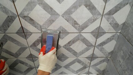 Grouting joints in the bathroom. Grouting ceramic tiles. Close-up of a hand in a protective glove holding a yellow trowel while grouting tiles.