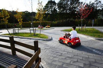 Young teenager boy driving a toy car on the road in the park.