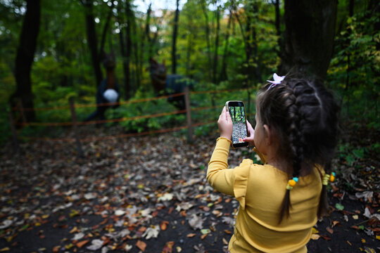 Little girl photographing autumn forest with a smartphone in the park.