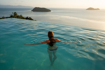 Girl in the pool among tropical palms and mountains at sunset