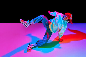 Athletic young man in motion, dancing breakdance isolated over black studio background in neon light. Concept of contemporary dance, street style, fashion, hobby, youth. Ad