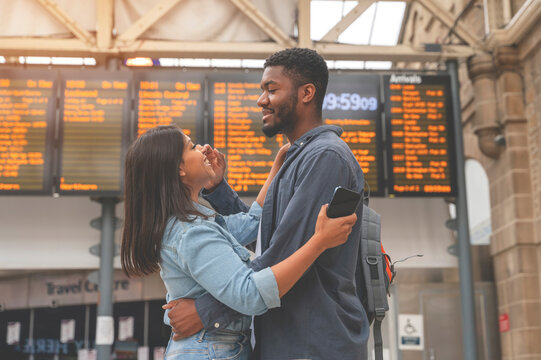 Happy man and woman in love meet and cuddle at a train station in front of the timetable toned image