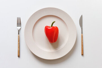 One red pepper in the dish. Fork and knife on white table. Vegan meal concept, diet concept