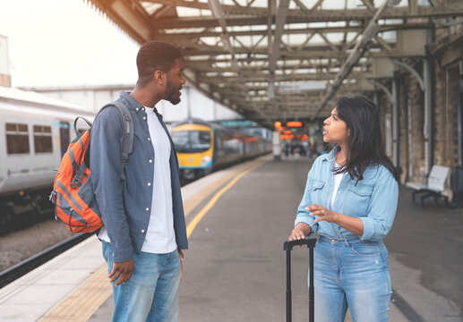 Man and woman are waiting for a train and talking at a railway station platform toned image