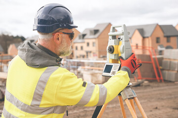 Surveyor builder site engineer with theodolite total station at construction site outdoors during surveying work - obrazy, fototapety, plakaty