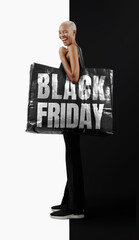 Black Friday Shopping. Stunning, joyful, smiling black woman in casual black outfit, holding a large black shopper bag with Black Friday text written on it. Background with copy space