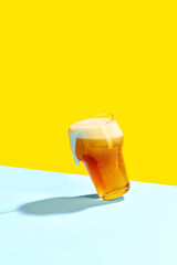 Tantalizingly mug of cold beer is placed on vibrant yellow and pastel blue background.
