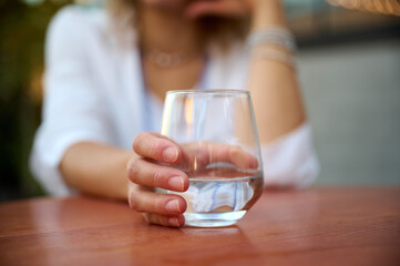 Portrait of a young attractive business woman sitting at a table in a cafe and holding a transparent glass of water. Close up view.