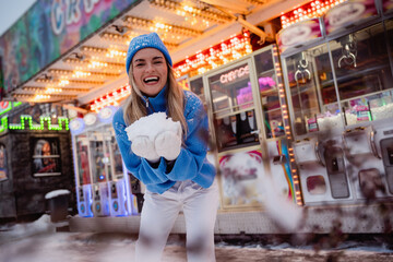 Fototapeta premium Cheerful and stylish woman, dressed in warm clothes, is having fun in a snowy winter amusement park