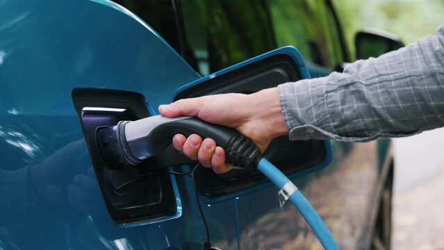 Close up Man plugging an electric car or EV at charging station at green. Save ecology alternative energy sustainable of future.