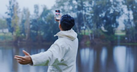 Happy man, video call and nature, rain and lake in outdoor adventure, social media influencer and travel or fitness blog. Selfie, live streaming and young person celebration in winter or forest river