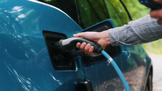 Close up Man plugging an electric car or EV at charging station at green. Save ecology alternative energy sustainable of future.