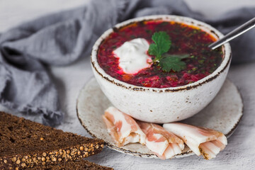 The concept of delicious food. Traditional Ukrainian, Russian borscht in a stylish ceramic plate with herbs, sour cream and garlic. Beetroot borscht with parsley, coriander and bacon with black bread.