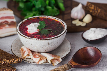 The concept of delicious food. Traditional Ukrainian, Russian borscht in a stylish ceramic plate with herbs, sour cream and garlic. Beetroot borscht with parsley, coriander and bacon with black bread.