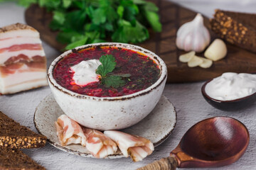 The concept of delicious food. Traditional Ukrainian, Russian borscht in a stylish ceramic plate with herbs, sour cream and garlic. Beetroot borscht with parsley, coriander and bacon with black bread.