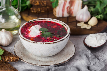 The concept of delicious food. Traditional Ukrainian, Russian borscht in a stylish ceramic plate with herbs, sour cream and garlic. Beetroot borscht with parsley, coriander and bacon with black bread.