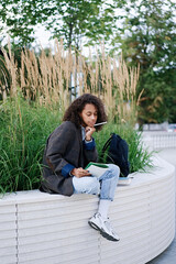 Young african american woman sitting on a bench and takes notes in a notebook. People, friendship, studying, lifestyle concept 