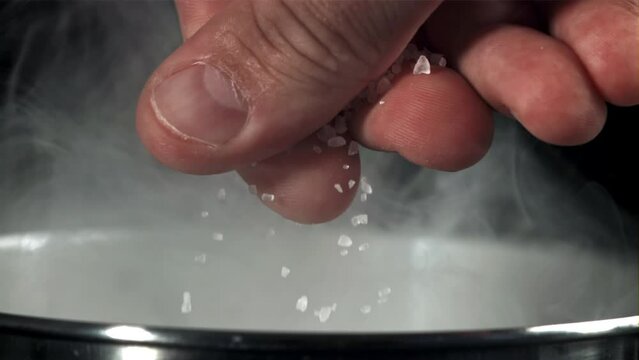 A man's hand salts water in a pan. Filmed on a high-speed camera at 1000 fps. High quality FullHD footage