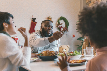 Portrait of young man with african american husband enjoying christmas lunch of turkey at decorated...