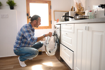 Young man taking laundry out of washing machine at home. Housekeeping, household and chores...