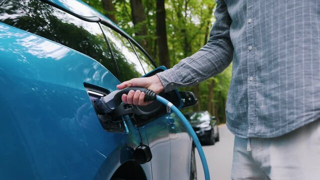 Man plugging an electric car or EV at charging station at green. Save ecology alternative energy sustainable of future.