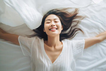 Young relaxed Asian woman resting in her bed with a smile. Top view - obrazy, fototapety, plakaty