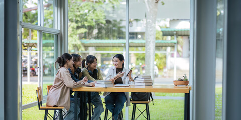 University students sitting together at table with book and laptop. Happy young people doing group study in college campus College and University life concept - obrazy, fototapety, plakaty