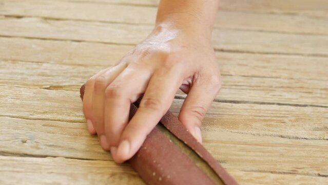 Close-up of a craftsman's hand polishing a wooden board with sandpaper. short hand of carpenter or joiner sanding wooden plank with sanding paper