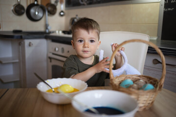 little cute boy paints eggs for easter sitting in the kitchen at the table