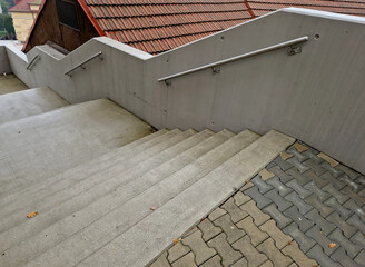 a staircase with concrete sides at a public building. the safe staircase has two handrails, one with a reduced height for children under 12 at the entrance to the school, brick, black, red. forgery